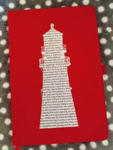 A picture of the notebook I use as a commonplace book: red, with a picture of a lighthouse in the middle.